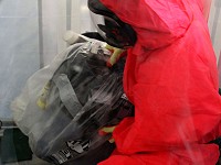 Remove  Asbestos operative entering an enclosure wearing red overalls and RPE