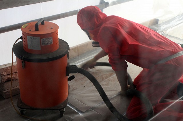 Asbestos Operative removing asbestos debris inside the enclosure with a vac, wearing full RPE and overalls